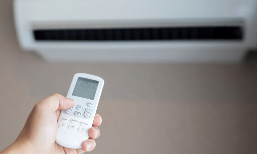 A hand using a remote to set an AC unit's temperature, a key action for applying energy efficient HVAC tips.