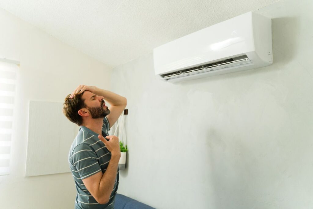 A frustrated man standing under his mini-split AC, a sign that he needs to know how to clean his mini split filter.