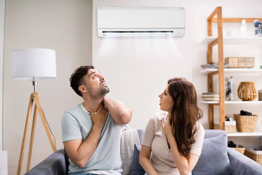 Sick couple with a cold and sore throat behind an AC, demonstrating that a defective AC can make you sick.