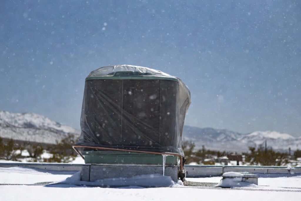 A swamp cooler on a rooftop, covered with an icicle with snowflakes falling, representing how to winterize a swamp cooler.