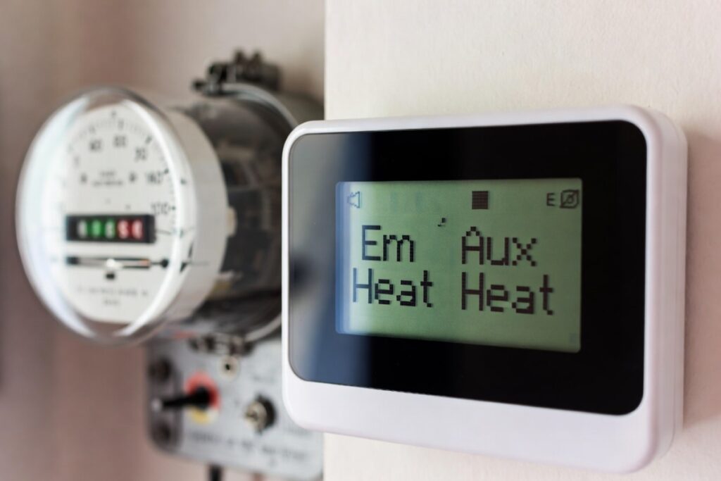 An AC thermostat screen displaying 'Em Heat' and 'Aux Heat", illustrating the emergency heat or auxiliary heat modes in AC.