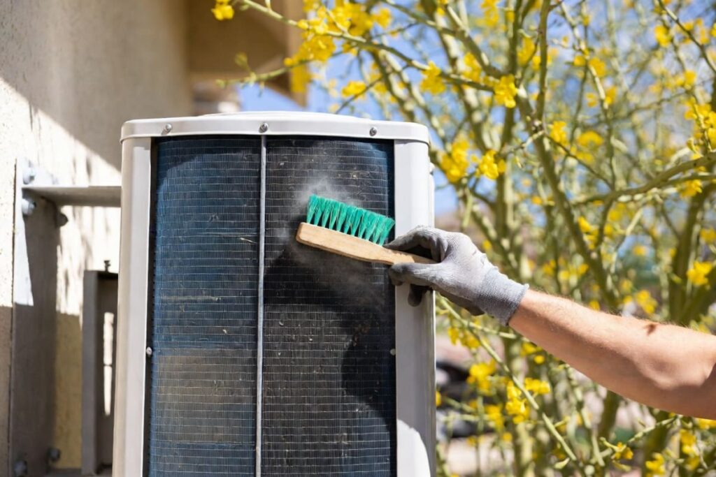 A technician brushes pollen from a suitcase-style unit during spring mini split maintenance in Lake Havasu.
