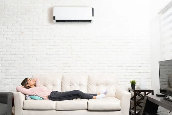 Woman sleeping on a couch below a quiet indoor unit, illustrating how to make air conditioner quieter for better rest.