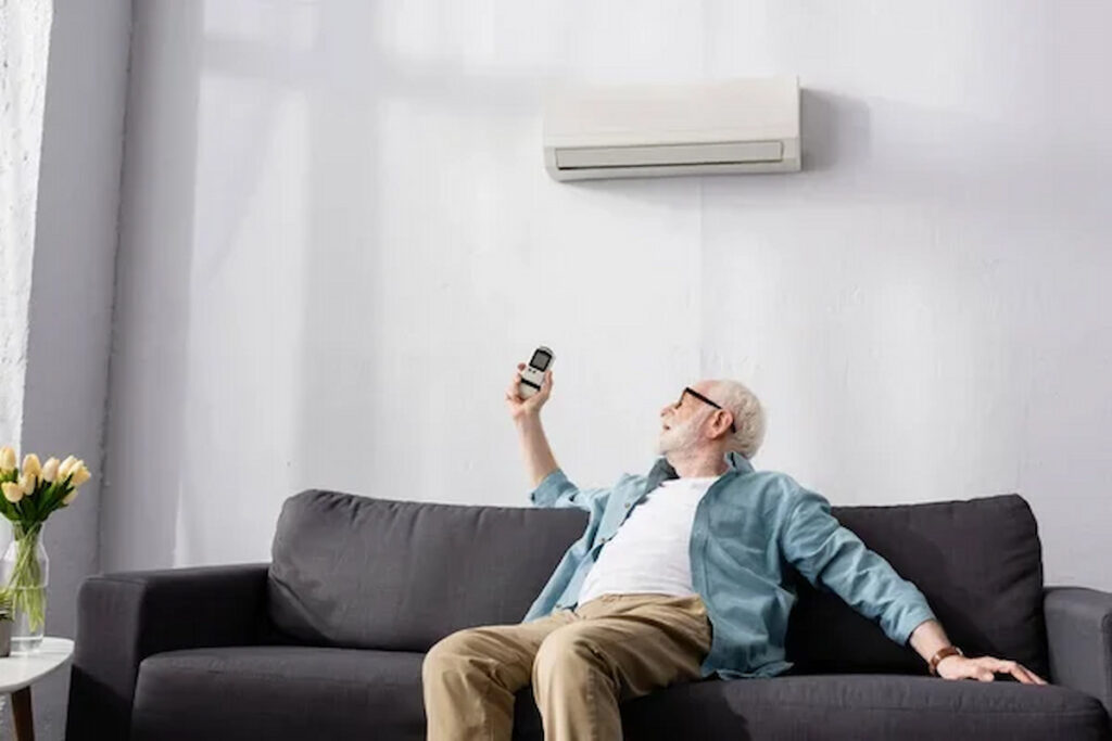 A man in a hot room with an AC remote, showing the importance of knowing why does an ac stop working when it's hot outside.
