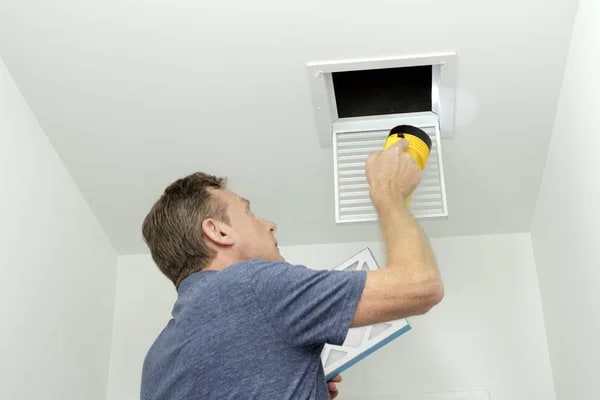 A technician inspects a ceiling vent to determine the best time to clean air ducts for improved home indoor air quality.